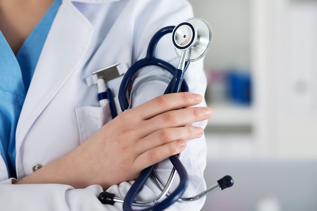 Closeup of female medicine therapeutist doctor standing with hands crossed on her chest holding stethoscope in office. Medical help or insurance concept. Physician is waiting for patient to examine