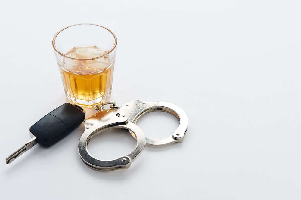 whiskey next to keys and a set of handcuffs on a white background