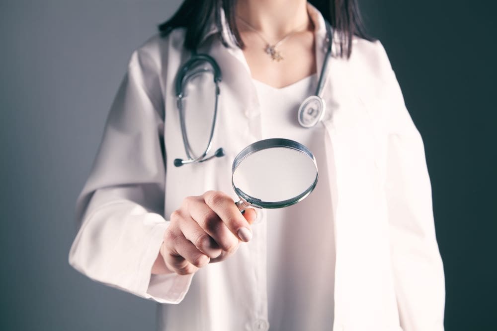 A female doctor holding up a magnifying glass to investigate something further.