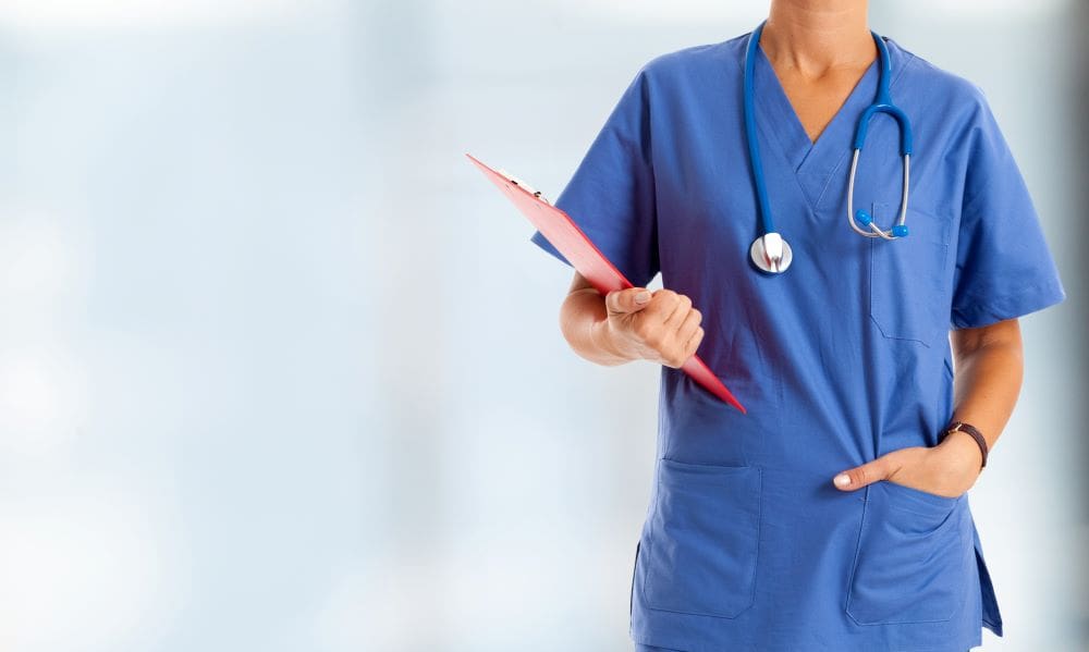 A nursing standing with a clipboard standing in front of a blurred background.